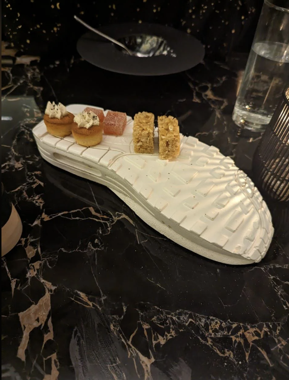 A unique dessert presentation, featuring assorted sweets arranged on a white, shoe-shaped platter, placed on a black marble table