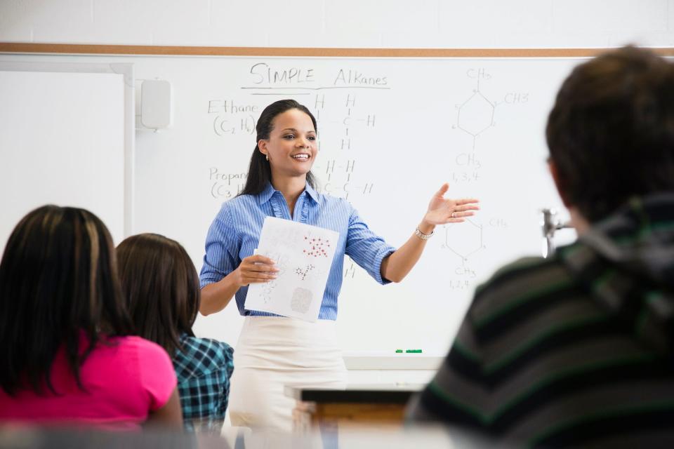 A teacher standing in front of a whiteboard while talking to students in a classroom