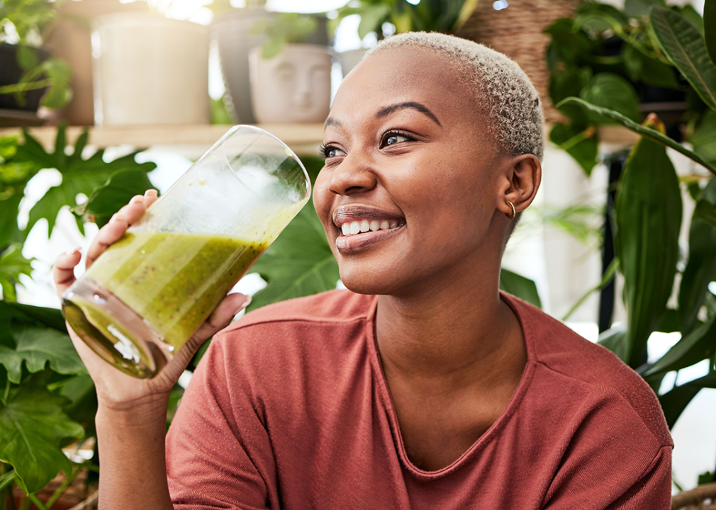 A smiling woman drinking a smoothie.