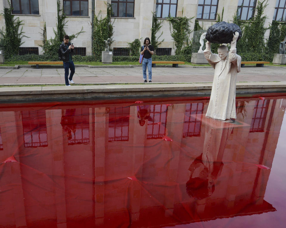 Visitors to the National Museum stop before a new statue of the late pope, St. John Paul II, throwing a stone at a "Poisoned Well" just hours before its official inauguration in the museum yard in Warsaw, Poland, Thursday, Sept. 24, 2020. The sculpture by Poland's Jerzy Kalina is said to be a response to a controversial 1999 sculpture by Italian Maurizio Cattelan in which the Polish-born pontiff was shown as being crushed by a similar stone. (AP Photo/Czarek Sokolowski)