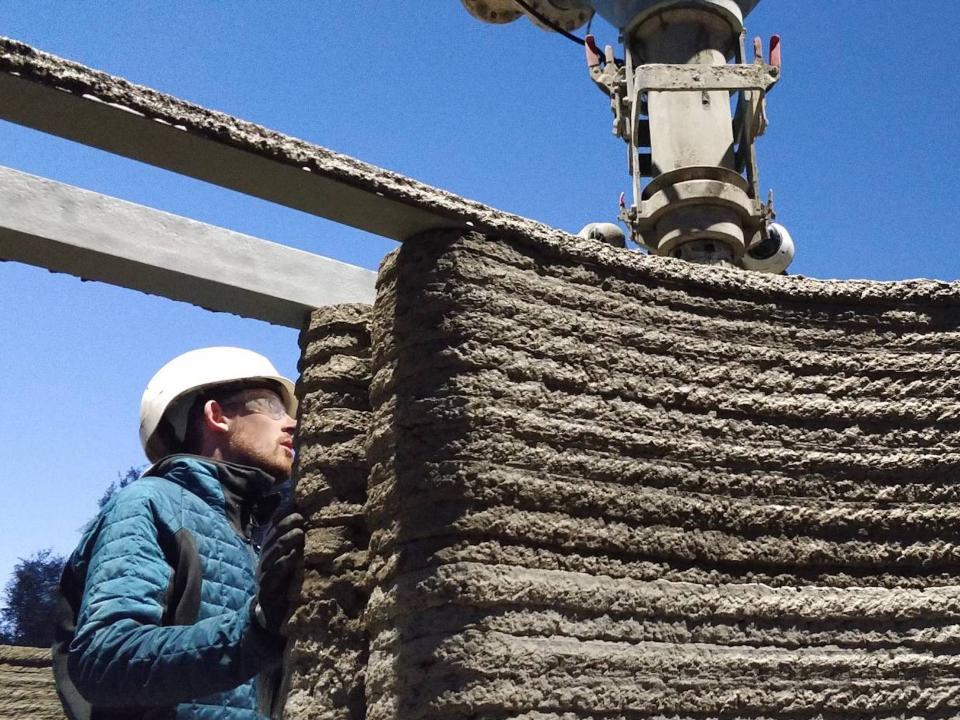 A person standing next to a 3D printed wall.