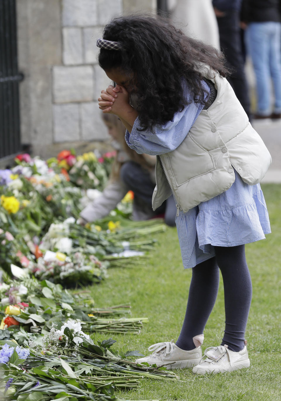 A child prays by the flowers left outside Windsor Castle in Windsor, England Sunday, April 11, 2021. Britain's Prince Philip, the irascible and tough-minded husband of Queen Elizabeth II who spent more than seven decades supporting his wife in a role that mostly defined his life, died on Friday. (AP Photo/Kirsty Wigglesworth)
