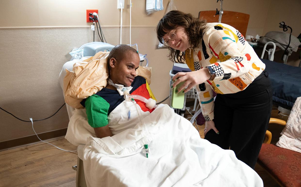 Lara Downing, right, shows Kassim Omar her reflection in the camera of her mobile phone. Downing is a social worker with Community Refugee and Immigration Services (CRIS) and for years has worked with Omar, who got shot in the neck and was paralyzed in 2022.