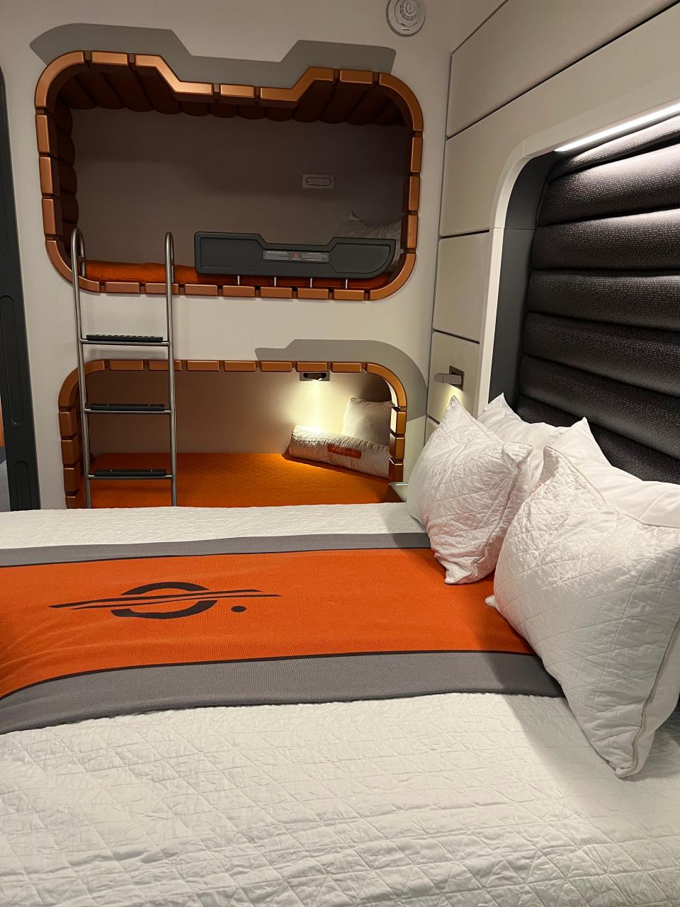 The interior of the Starcruiser room with white sheets and an orange design on top and bunk beds built into the wall