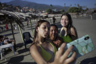 Friends take photos of themselves on La Ultima beach which was reopened this week after it was closed for months amid the COVID-19 pandemic in La Guaira, Venezuela, Friday, Oct. 23, 2020. Strict quarantine restrictions forced the closure of beaches across the country in March and reopened this week in hopes of revitalizing the battered economy. (AP Photo/Matias Delacroix)