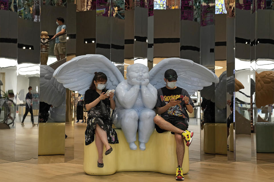 A couple wearing face masks to help curb the spread of the coronavirus sit on an angel statue browsing their smartphones at a shopping mall in Beijing, Sunday, June 6, 2021. (AP Photo/Andy Wong)