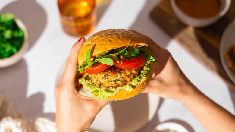 hands holding salmon guacamole burger with tomatoes