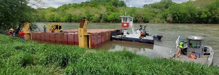 A tug boat moves a construction barge from Dam. 4, where it had been stuck since breaking loose from its mooring on the Potomac River over the weekend following heavy rain.