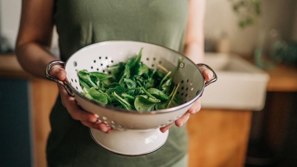 green vegan breakfast meal in bowl with spinach, arugula, avocado, seeds and sprouts girl in leggins holding plate with hands visible, top view clean eating, dieting, vegan food concept