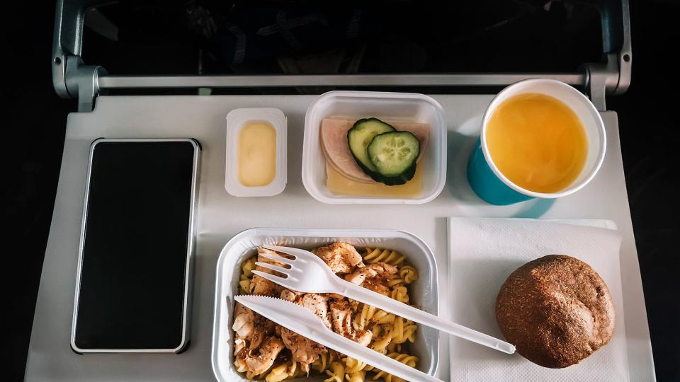 Inflight meal service tray for economy class, meat with pasta, seasoning fruit, salad, cucumber, a glass of juice and butter