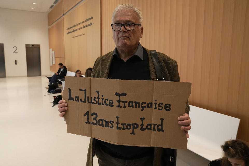 A man holds a placard reading "The French justice, 13 years too late" prior to the start of the trial of Airbus and Air France companies, at the Paris courthouse, in Paris, Monday, Oct. 10 , 2022. Airbus and Air France go on trial on manslaughter charges Monday over the crash of a Rio-Paris flight in 2009 that plunged into the Atlantic amid thunderstorms. The accident kiled all 228 people aboard and led to changes in air safety regulations. (AP Photo/Michel Euler)