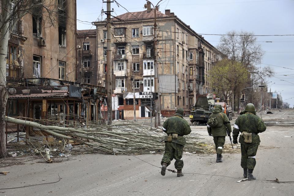 FILE - Servicemen of the militia from the Donetsk People's Republic walk past damaged apartment buildings near the Illich Iron & Steel Works Metallurgical Plant, the second-largest metallurgical enterprise in Ukraine, in an area controlled by Russian-backed separatist forces in Mariupol, Ukraine, Saturday, April 16, 2022. Mariupol, which is part of the industrial region in eastern Ukraine known as the Donbas, has been a key objective for Russia since the start of the Feb. 24 invasion. (AP Photo/Alexei Alexandrov)