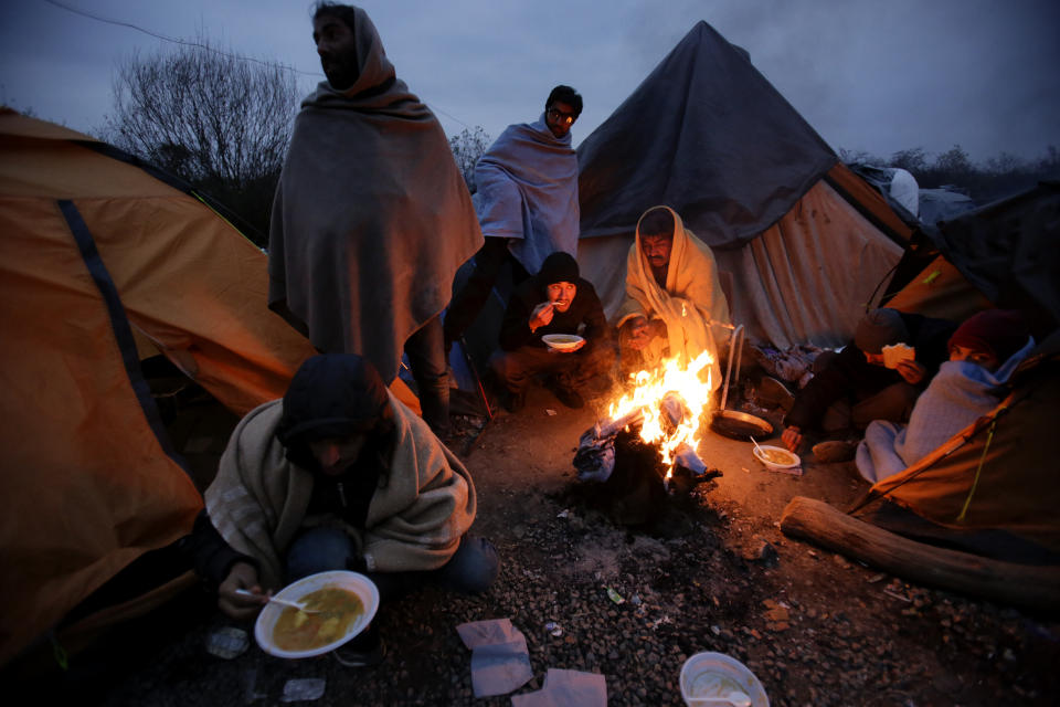In this Sunday, Nov. 18, 2019 photo migrants eat around a fire at a camp in Velika Kladusa, Bosnia, close to the border to Croatia. The approach of the tough Balkan winter spells tough times for the migrants that remain stuck in the region while trying to reach Western Europe, with hundreds of them staying in make-shift camps with no heating or facilities.(AP Photo/Amel Emric)