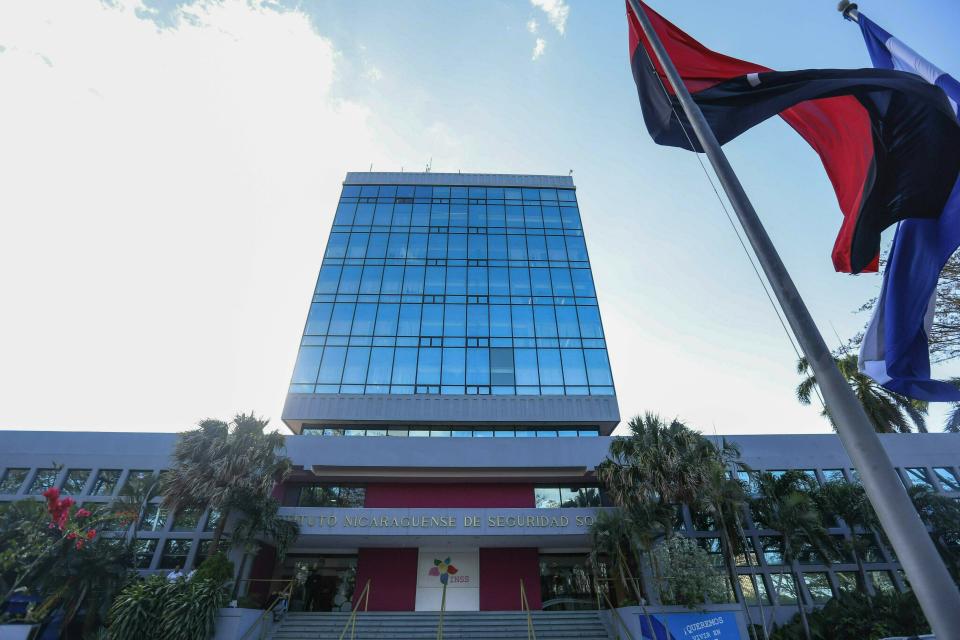 En esta foto del 8 de febrero de 2019 una bandera del partido gobernante Frente Sandinista de Liberación Nacional y una bandera nacional vuelan fuera del Instituto de Seguridad Social, en Managua, Nicaragua. Un nuevo plan para reducir los pagos de pensiones y aumentar los aportes de los empleados está en vigencia en el país centroamericano. Economistas y empresarios advierten que amenaza con tener efectos aún más graves para los nicaragüenses y que sumarán al país en una recesión más profunda y en el desempleo. (AP Foto / Alfredo Zuniga)