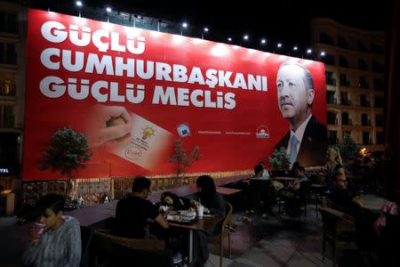 People sit in a restaurant terrace as a pre-election poster depicting Turkish President Tayyip Erdogan reads "Strong President, strong parliament", in Istanbul, Turkey, June 20, 2018. REUTERS/Alkis Konstantinidis
