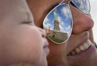 The Statue of Liberty is reflected in the glasses of Katie Ullman as she points to it while she holds her one-year-old son Tyler in her arms on Liberty Island in New York, October 13, 2013. REUTERS/Carlo Allegri