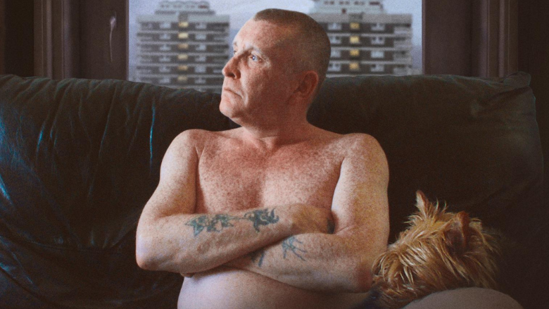  Joe McNally in The Flats pictured topless on sofa with dog and New Lodge flats visible through window behind him