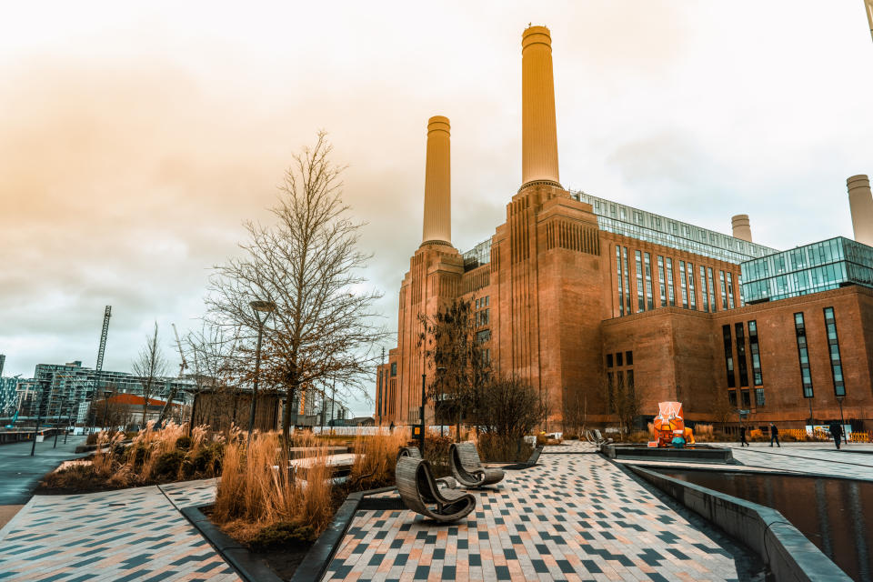 Battersea Power Station in London is shown with its iconic chimneys, modernized surrounding area, and a mix of industrial and contemporary architecture