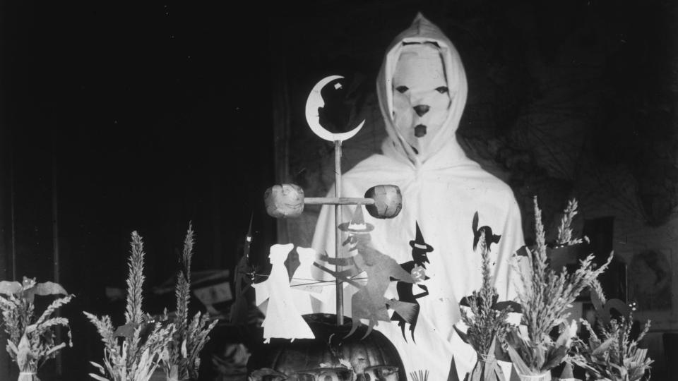 <p>A person dressed as a ghost circa 1905 surrounded by Halloween decorations in a rural schoolhouse. </p>
