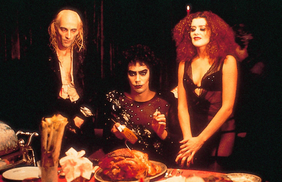 Richard O'Brien and Patricia Quinn stand around Tim Curry