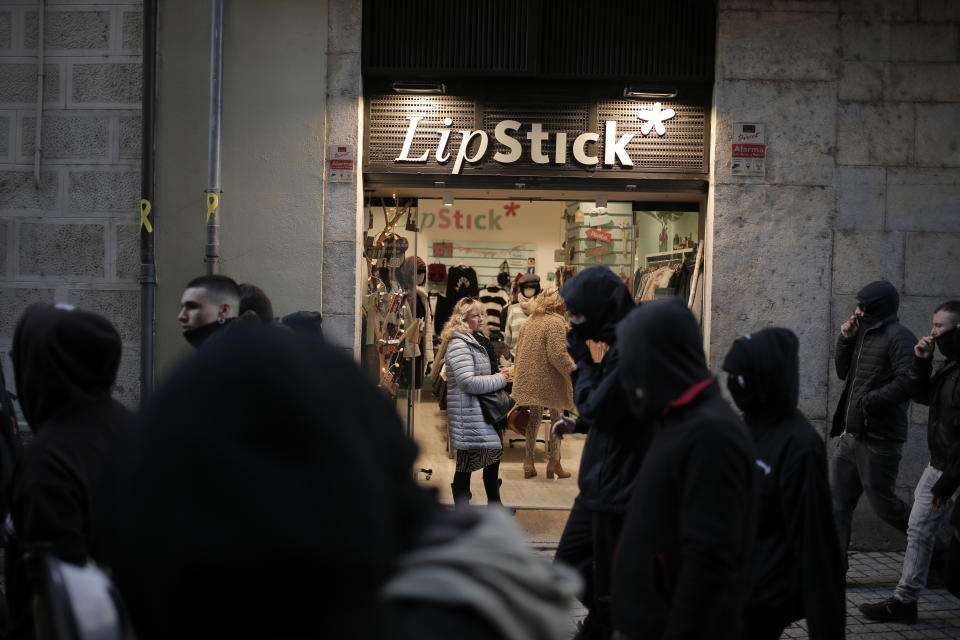 A woman looks out from a store as demonstrators walk past during a protest against the presence of the far-right party VOX who held a meeting on Constitution Day in Girona, Spain, Friday Dec. 6, 2019. The biggest change emerging from the Nov. 10 election was the resurgence of extreme Spanish nationalism in the form of the far-right Vox party that won 52 seats to become Spain's third parliamentary force. (AP Photo/Joan Mateu)