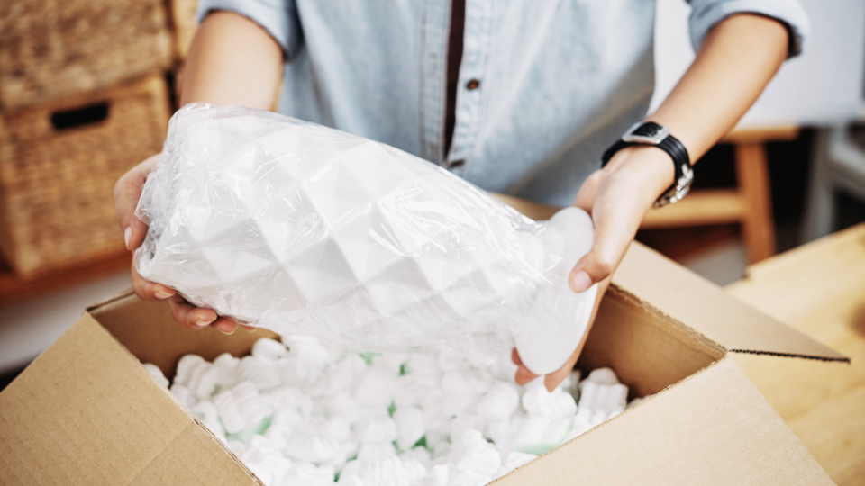 Woman puts a fragile vase in a box with packing peanuts. - DragonImages/iStockphoto
