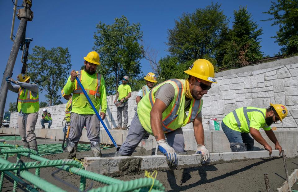 GM & Sons construction workers smooth out the poured concrete on a link between Mount Elliott Park and the MacArthur Bridge in Detroit on Thursday, Aug. 10, 2023.