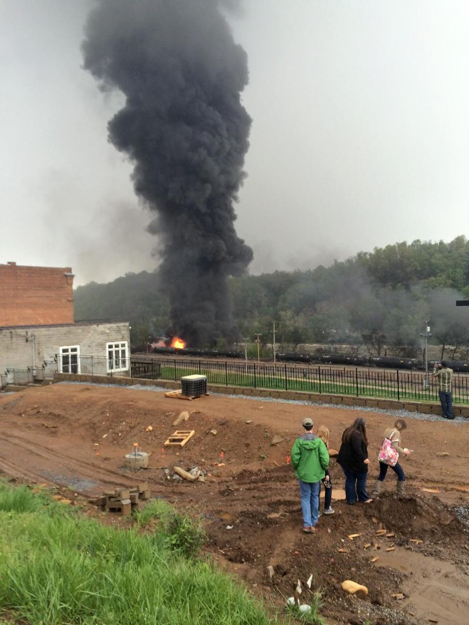 In this mobile phone photo provided Charles Peters, people look on as smoke rises after several CSX tanker cars carrying crude oil derailed on Wednesday, April 30, 2014, in Lynchburg, Va. Authorities evacuated numerous buildings Wednesday after the derailment. (AP Photo/Charles Peters) MANDATORY CREDIT