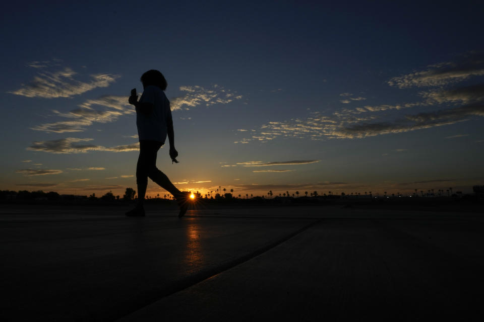 Janice Edwards listens to a podcast on her phone as she walks at sunrise Tuesday, July 11, 2023, in Yuma, Ariz. Edwards takes her walks starting before dawn to avoid the heat. Even desert residents accustomed to scorching summers are feeling the grip of an extreme heat wave smacking the Southwest this week. Arizona, Nevada, New Mexico and Southern California are getting hit with 100-degree-plus temps and excessive heat warnings. (AP Photo/Gregory Bull)