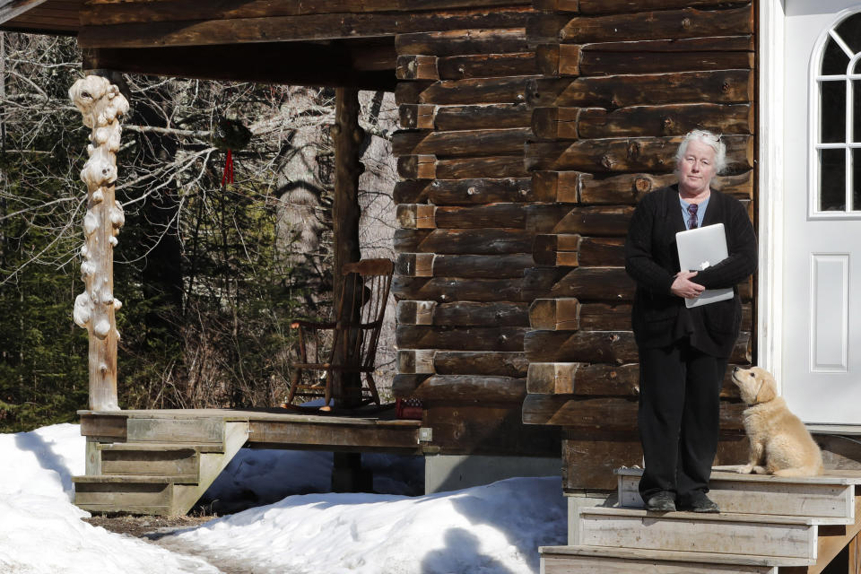 Julie Dolan, chair of her town's Broadband Committee, poses with her computer on the steps of her family's rural home in Sandwich, N.H., Thursday, March 26, 2020. In the town of 1,200 best known as the setting for the movie “On Golden Pond," broadband is scarce. Forget streaming Netflix, much less working or studying from home. Even the police department has trouble uploading its reports. (AP Photo/Charles Krupa)