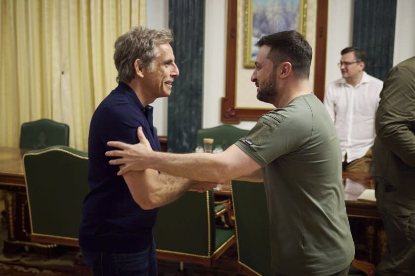 A man in a blue shirt shaking hands with another man in a green shirt