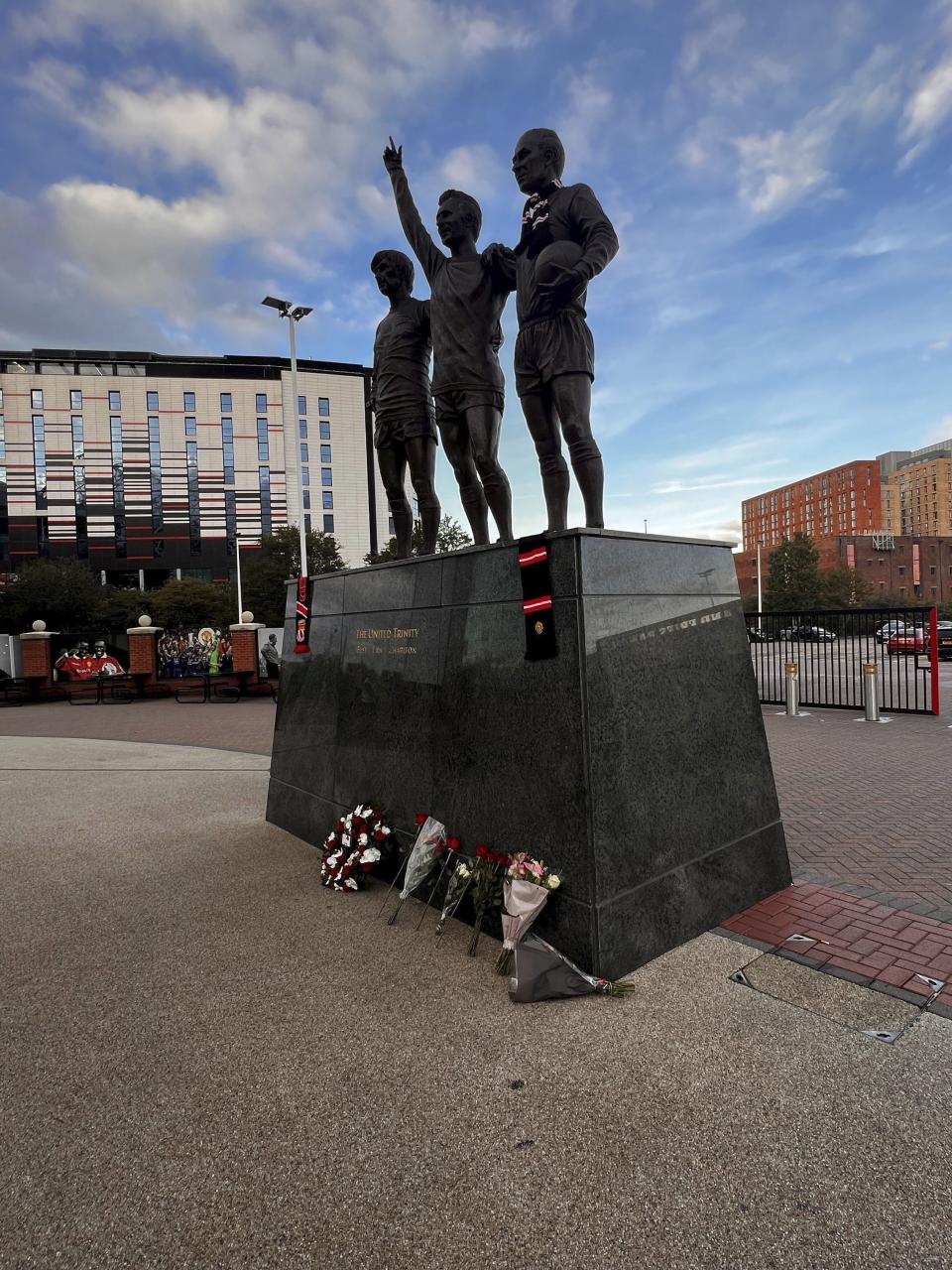 La gente coloca flores y tributos frente a la estatua The United Trinity para recordar a Bobby Charlton, quien falleció el sábado 21 de octubre del 2023 a los 86 años. (Steven Allen/PA via AP)