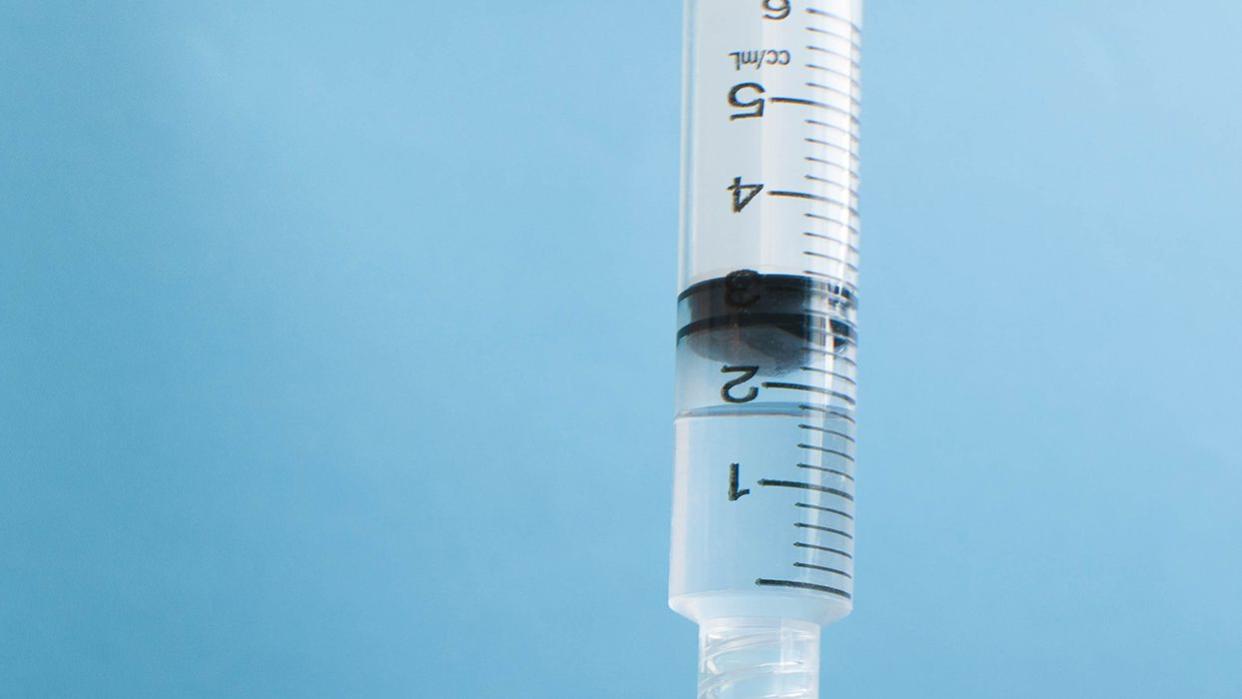 A syringe is injected into a vial against blue background