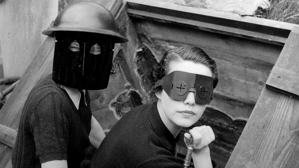 Models pose for Vogue by an air raid shelter in London during the Blitz, wearing masks worn to protect against incendiary bombs. - Lee Miller Archives, England 2023