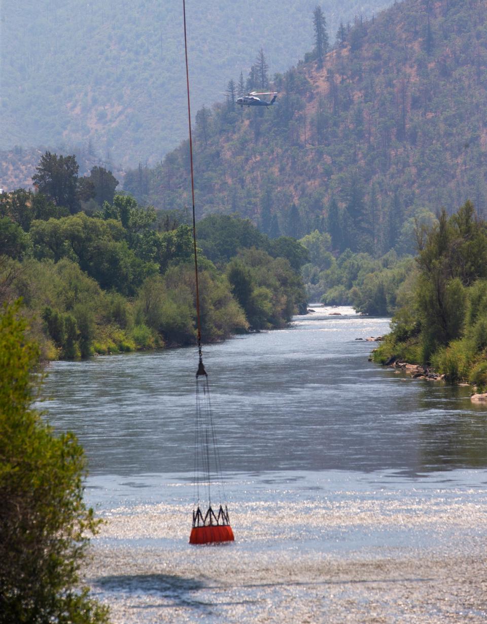 A helicopter drops its water bucket into the Klamath River while another helicopter hovers upstream as a weather inversion lifts over the McKinney Fire northwest of Yreka, allowing firefighters to attack the fire from the air on Tuesday, Aug. 2, 2022.