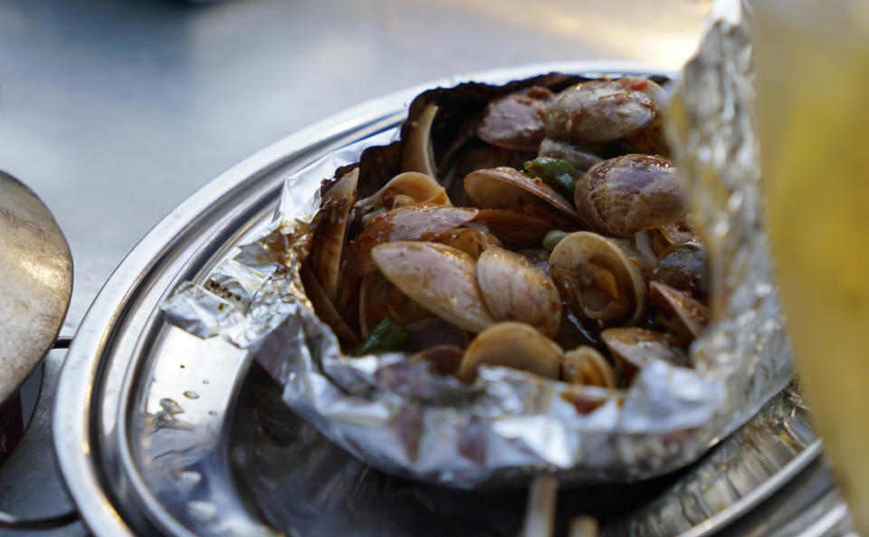 A close-up of a serving of clams cooked in foil, garnished with herms and spices, arranged on a metal plate