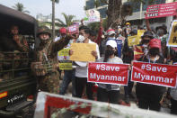 Protesters hold signs that read "#Save Myanmar" next to soldiers deployed outside the Central Bank of Myanmar building in Yangon, Myanmar on Monday, Feb. 15, 2021. Myanmar's military leaders have extended their detention of Aung San Suu Kyi, whose remand was set to expire Monday and whose freedom is a key demand of the crowds of people continuing to protest this month's military coup. (AP Photo)