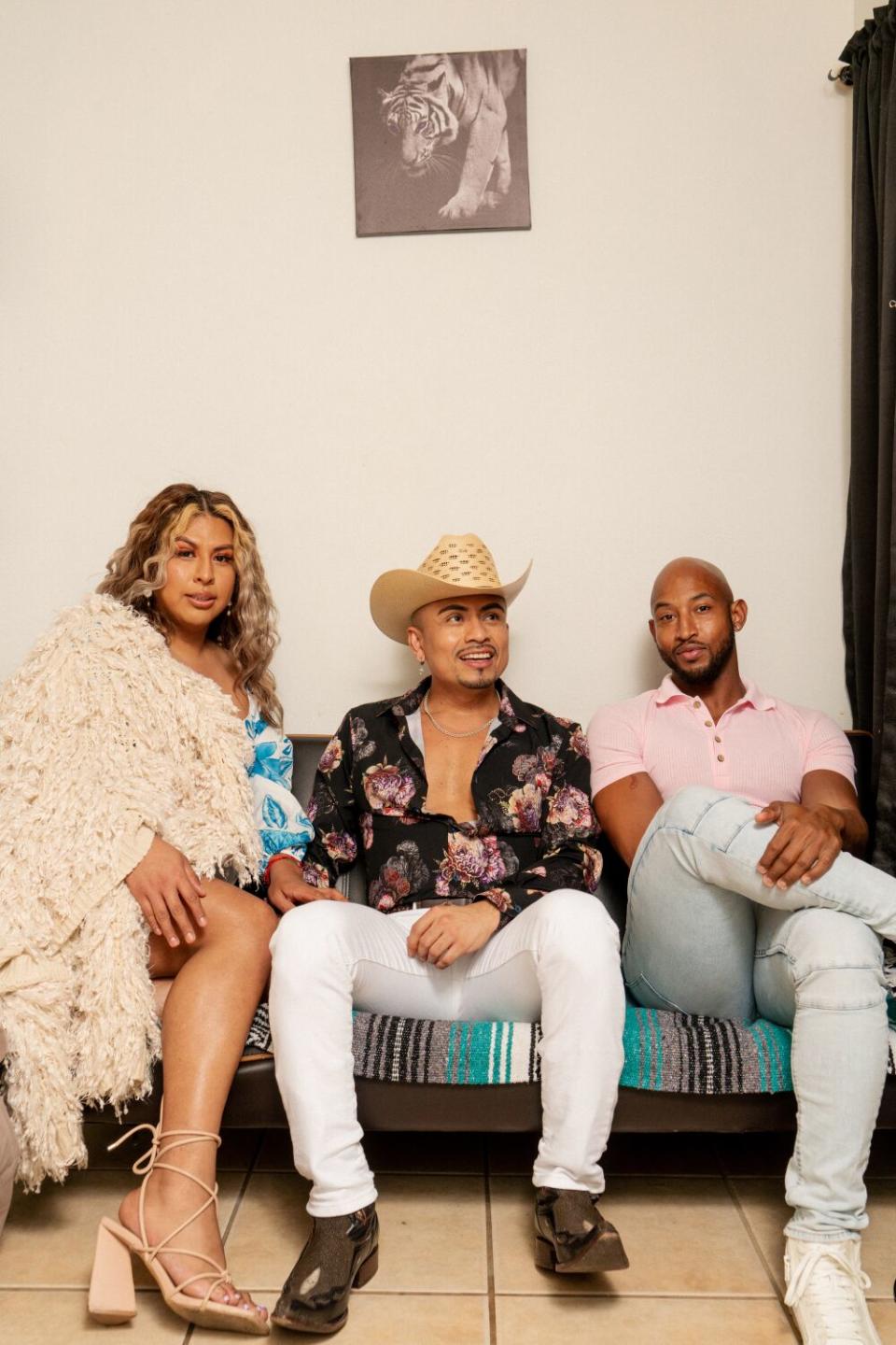 Three people sitting on a serape-covered couch.