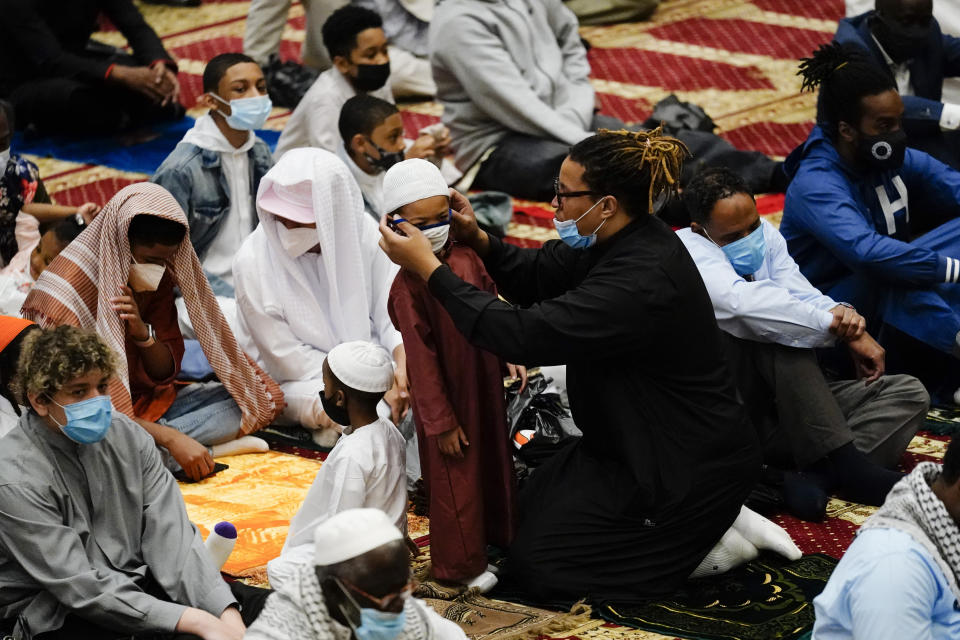 A worshipper helps a child with a mask before he and others perform an Eid al-Fitr prayer at the Masjidullah Mosque in Philadelphia, Thursday, May 13, 2021. Millions of Muslims across the world are marking the holiday of Eid al-Fitr, the end of the fasting month of Ramadan. (AP Photo/Matt Rourke)