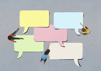 Seen from above, three kids arrange big paper speech bubbles on the ground.