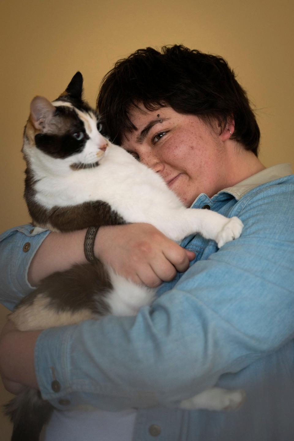 Lee Sanchez, 23, holds their family cat named Willow at their home in Grand Haven on Tuesday, April 18, 2023. "It was a thing that hit me really gradually and then all at once," said Sanchez, while reflecting back on moments that led to discovering they are autistic. "I had a meltdown one day. Then there was a lot of pausing and learning and reflecting."