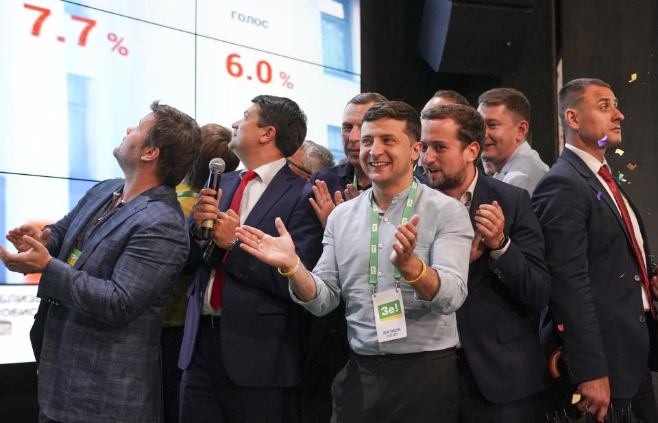 Ukrainian President Volodymyr Zelenskiy, center, applauds with his team as they look at the election results at his party's headquarters after a parliamentary election in Kiev, Ukraine, Sunday, July 21, 2019. Zelenskiy's party took the largest share of votes in the country's snap parliamentary election, an exit poll showed Sunday. (AP Photo/Evgeniy Maloletka)