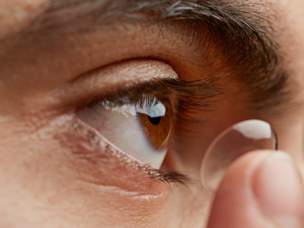 A close-up of a man with brown eyes putting in contact lens with the tip of his finger