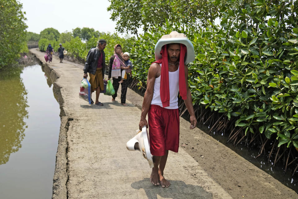 Aslori carries toilets he recovered from his and a relative's house, as he and several neighbors return from visiting their old abandoned houses in Mondoliko, Central Java, Indonesia, Monday, Sept. 5, 2022. He and his family moved to drier land, becoming climate migrants as many of their neighbors had before them. (AP Photo/Dita Alangkara)