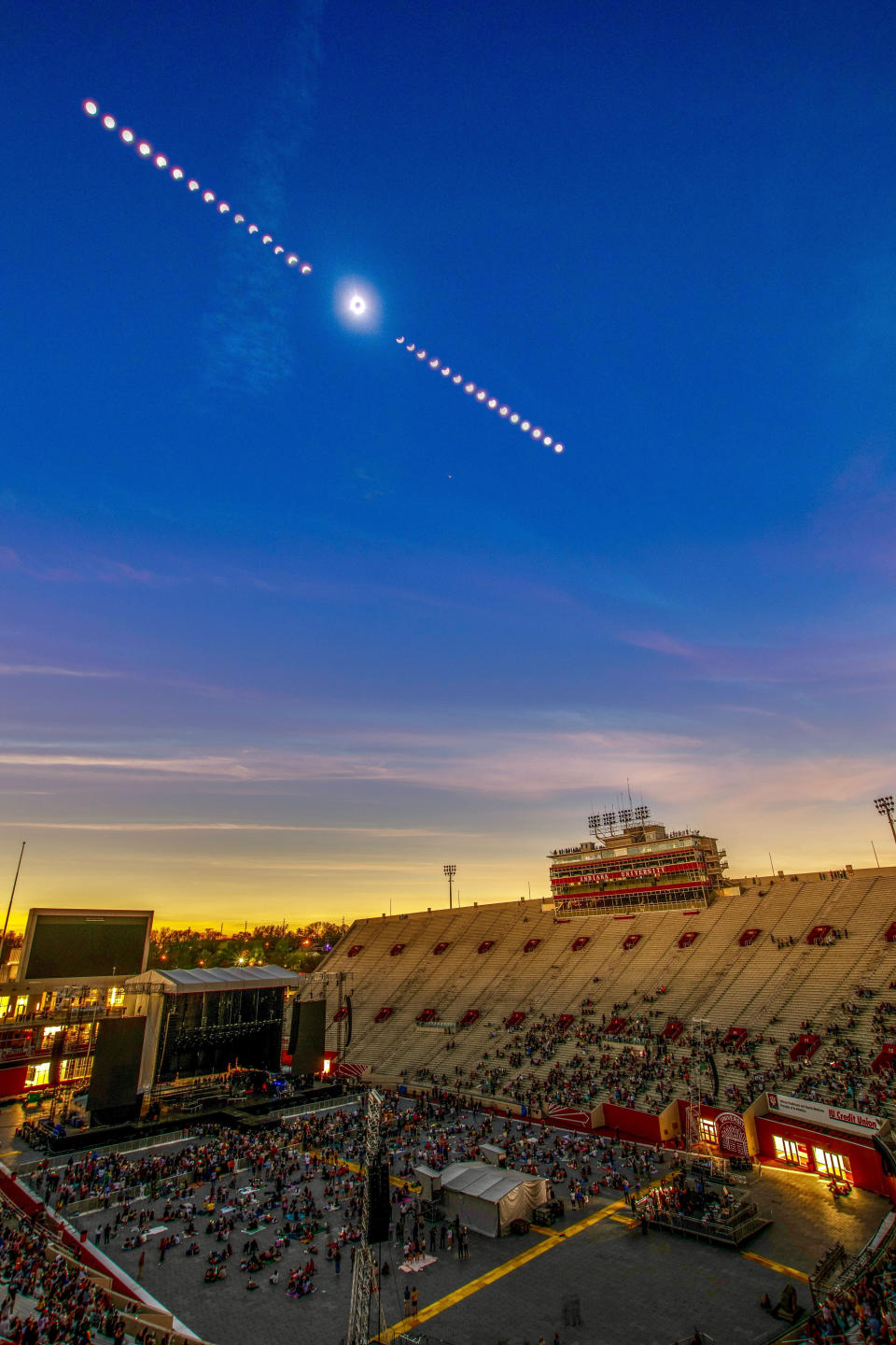 An eclipse time-lapse composite image shows the progress of a solar eclipse, framing totality in the center in a dark sky above a sparsely populated Indiana University football stadium.