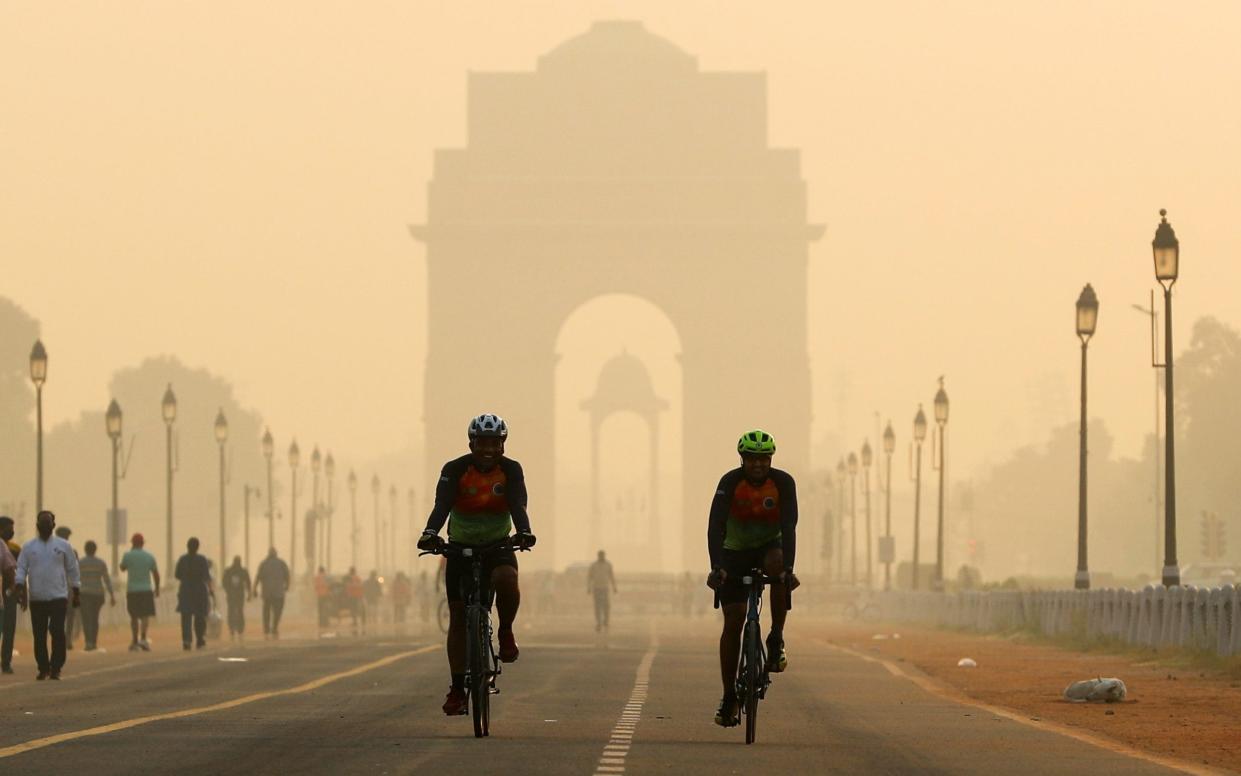 Men ride their bicycles in front of the India Gate shrouded in smog, in New Delhi, India