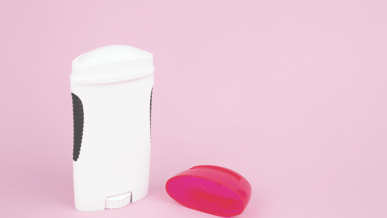 An open white stick of deodorant with its red cap next to it before a pink background