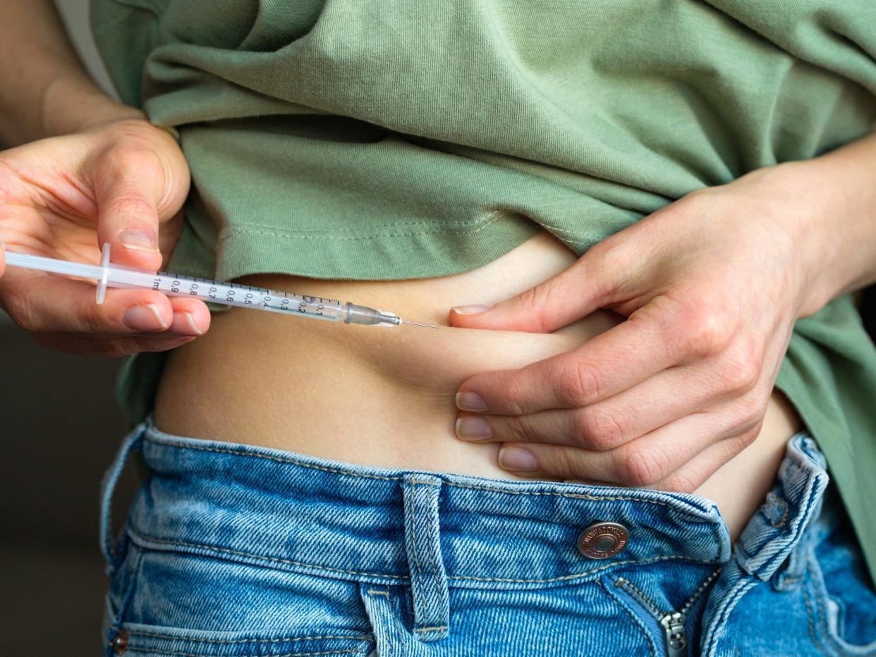 a person injecting medication with a syringe into the skin of their stomach