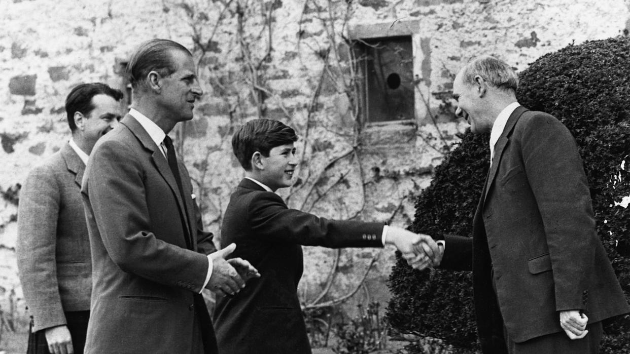 King Charles shaking hands with a headmaster with Prince Philip by his side