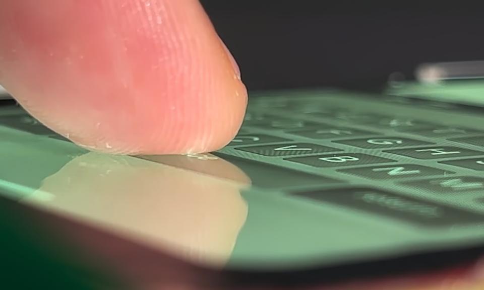 Closeup of a finger touching an inflated space bar on a protruding onscreen keyboard on a smartphone.